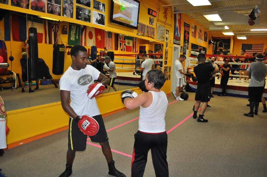 Roy Wayne holding focus mitts while coaching a boxer in the gym